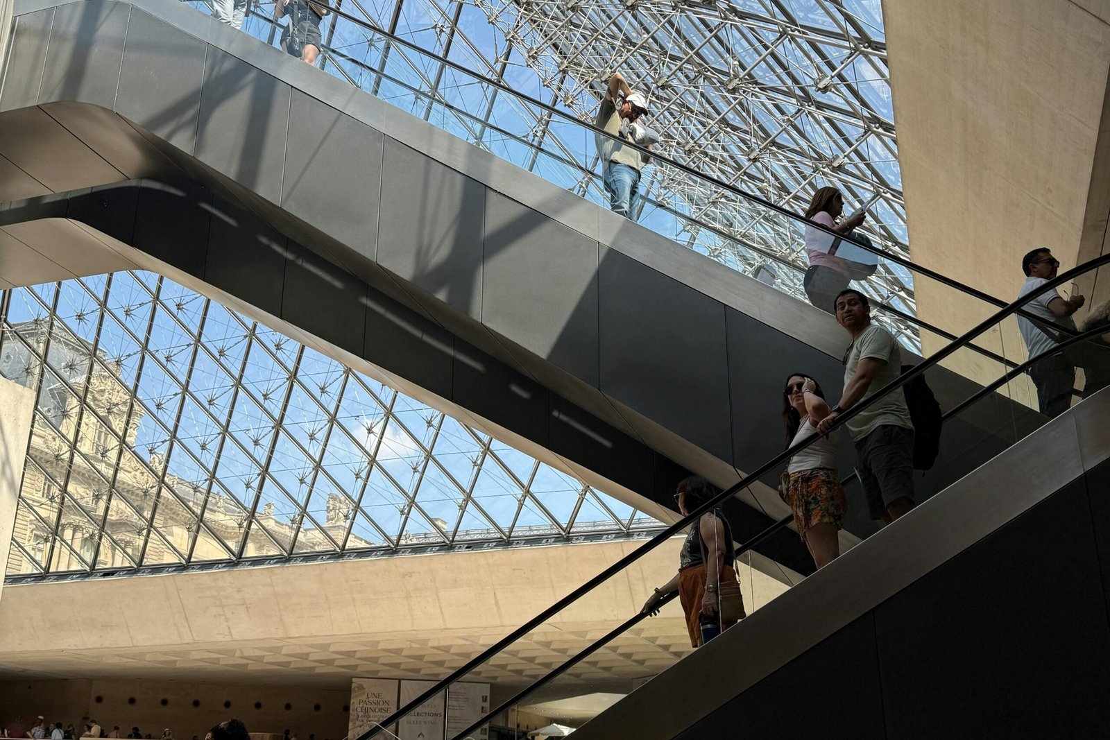 People using escalators beneath the glass pyramid at the Louvre Museum, Paris.