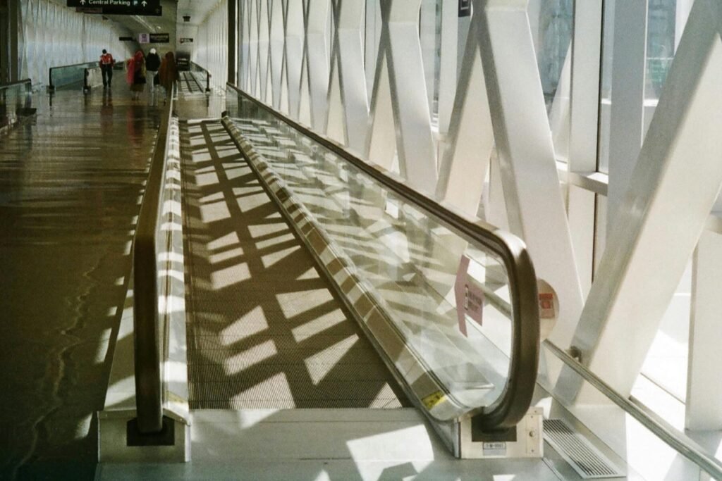 Bright airport corridor featuring a moving walkway and geometric architecture.